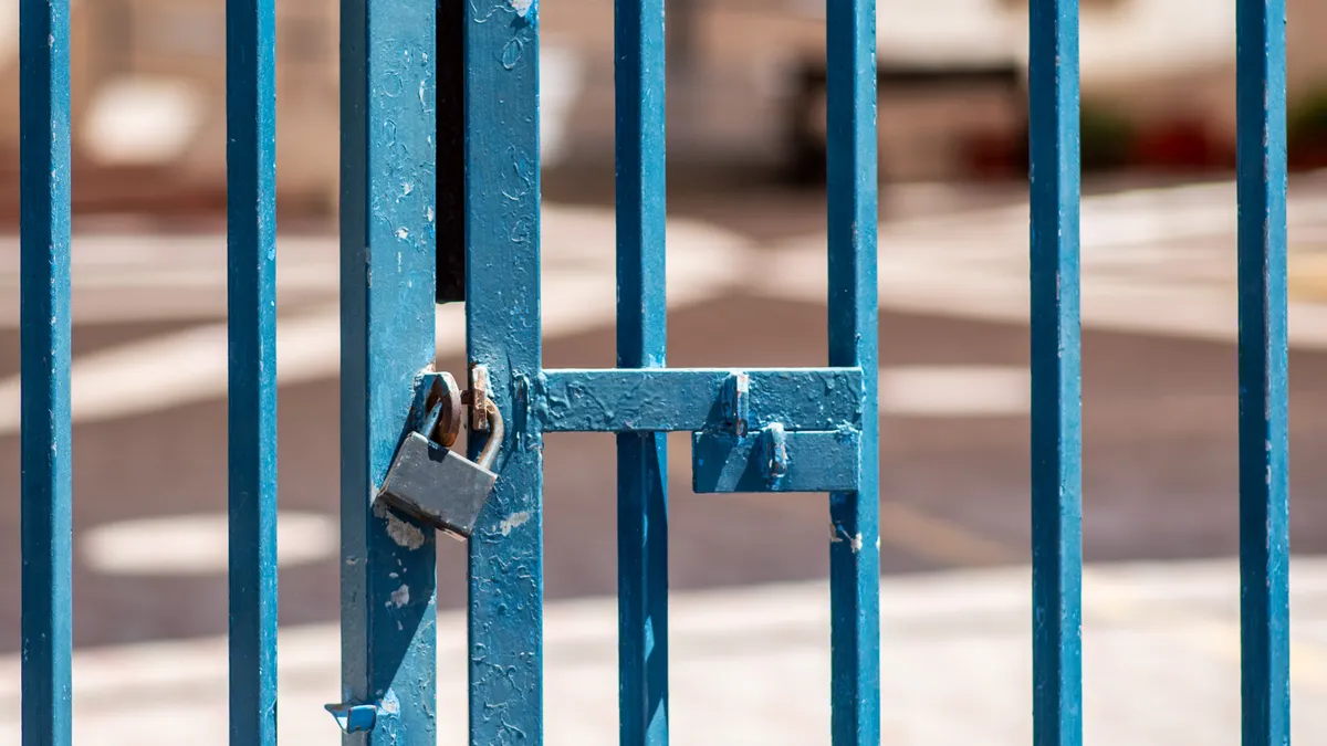 A locked gate is visible in front of a blurred background.