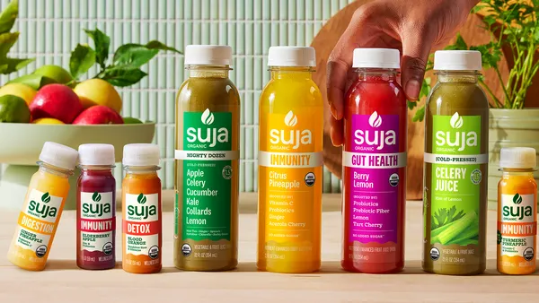 Small and large bottles of Suja wellness drinks are lined up on a counter and a hand reaches in to grab one.
