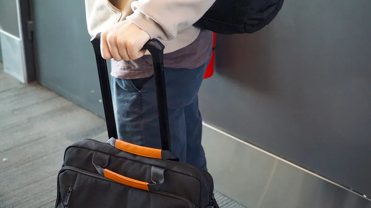 A hand holds on the extended handle of a rolling suitcase.