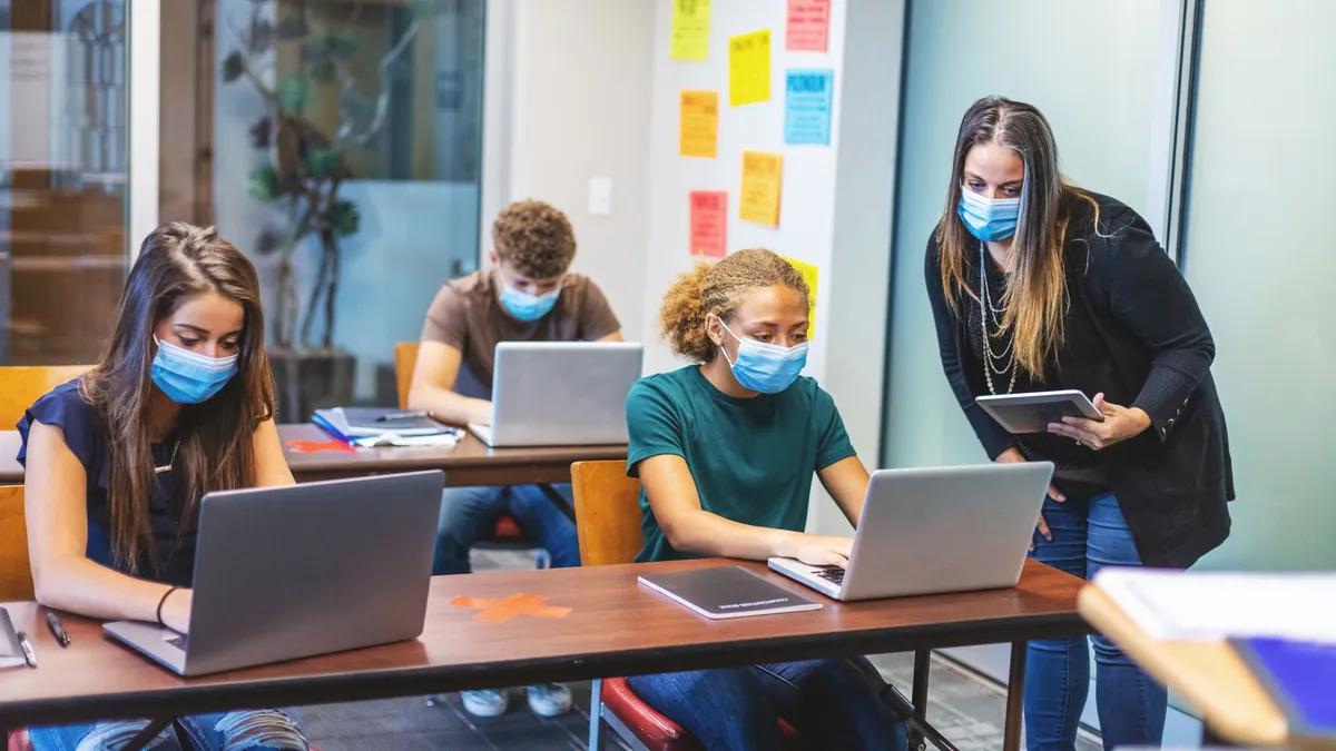 High School Students and Teacher wearing face masks and social distancing in Classroom Setting working on laptop technology - stock photo