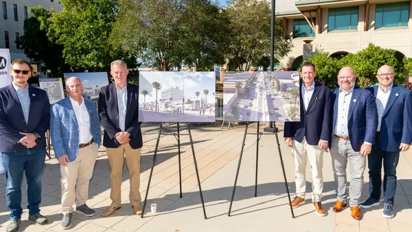 A group of people pose for a photograph along with easels with renderings of a future construction project.