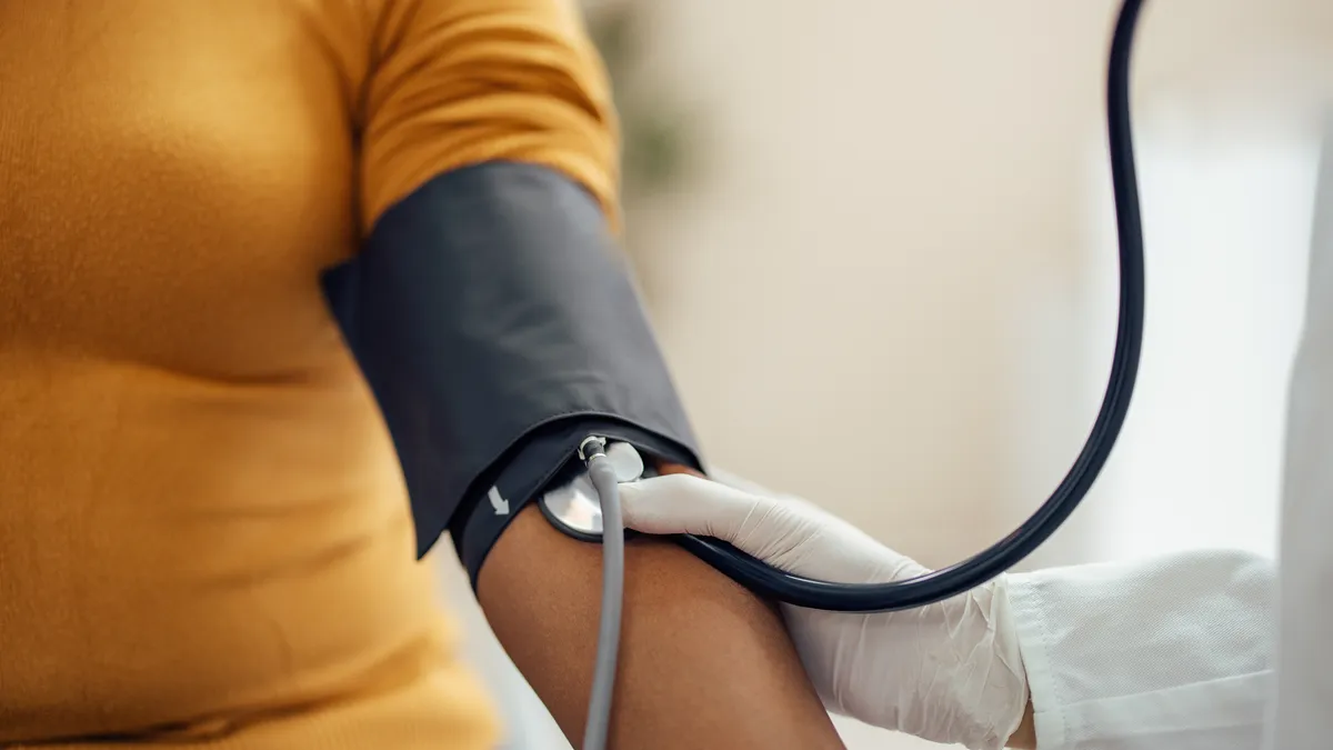 A person wears a blood pressure cuff on their upper arm while another person holds a stethoscope to their arm.