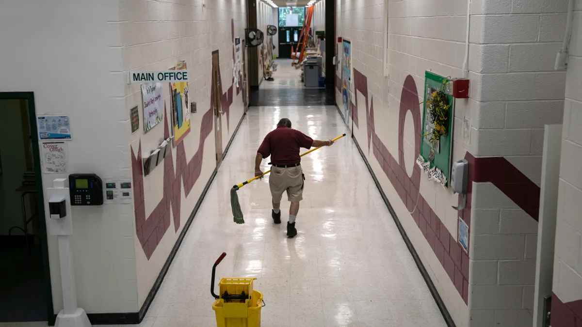 School maintenance staff walks down a hallway with a mop in hand