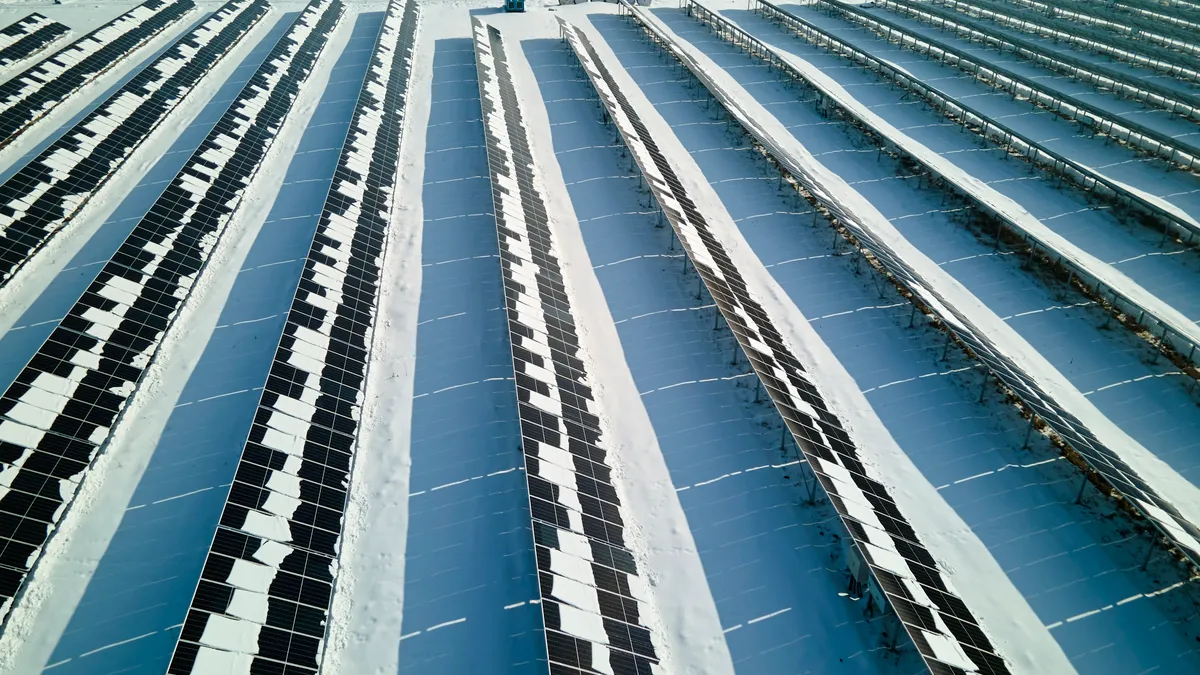 An aerial view of a solar farm with snow-covered solar panels.