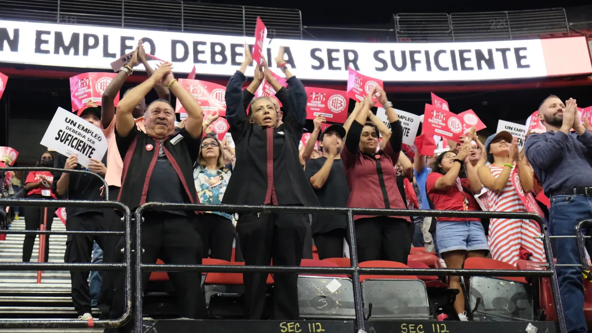 Workers hold picket signs as they stand in stadium rafters.