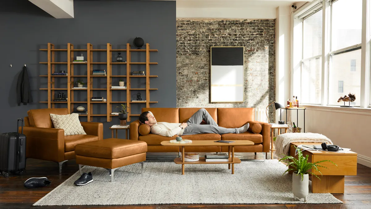 A living room with a person laying down on a tan sofa