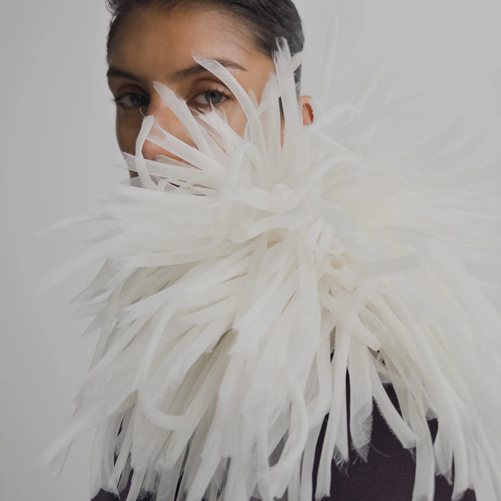 Person peeks at the camera behind a head-sized silk dahlia flower pin by Phoebe Philo.