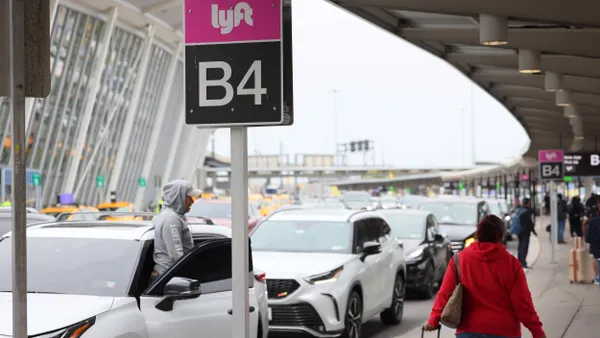 Two people in the foreground under an overhang alongside a line of cars.