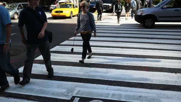 People walking in a marked crosswalk with cars around them.
