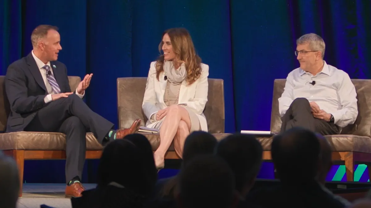 Three people speak on stage at a conference.