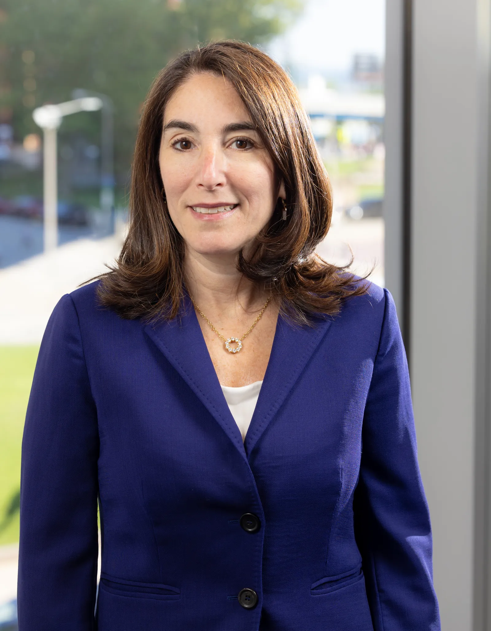 Beth Hammack poses for a photo standing in front of a window wearing a blue jacket