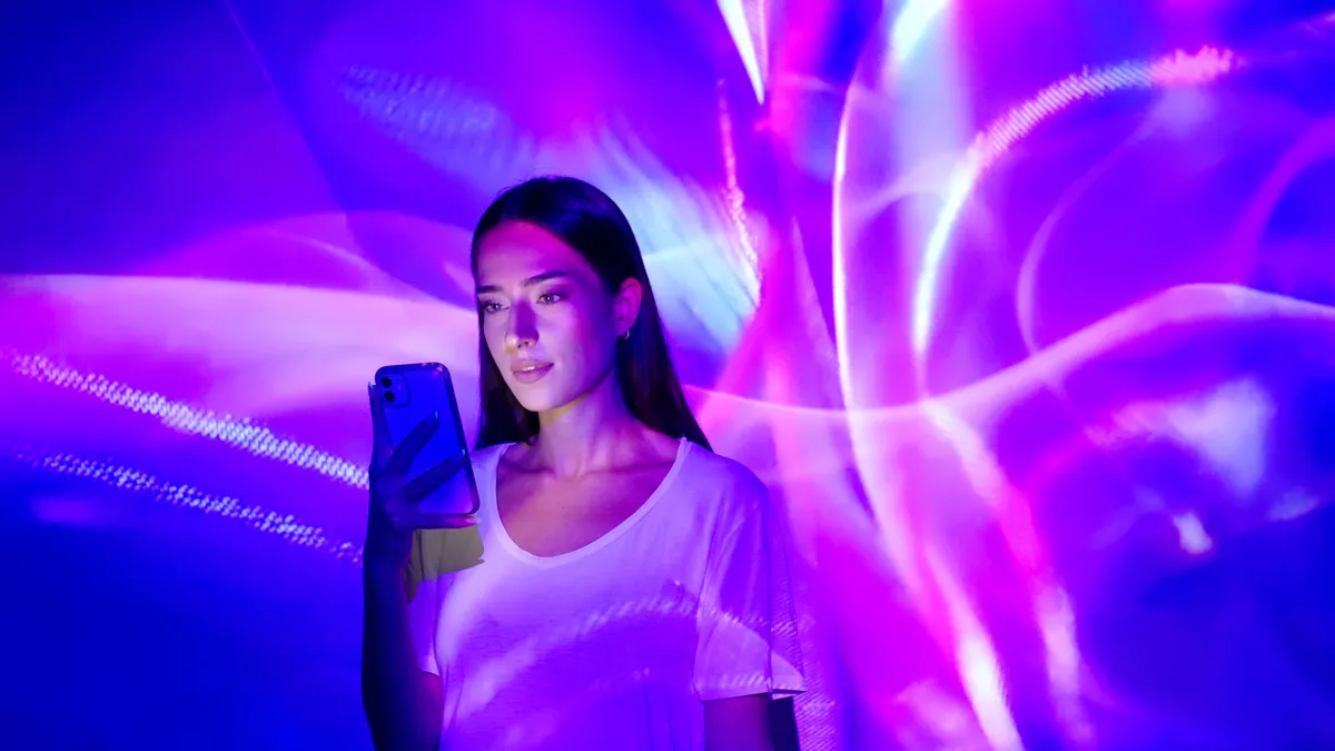 A person looks at their smartphone screen in a room lit by colorful neon lights.