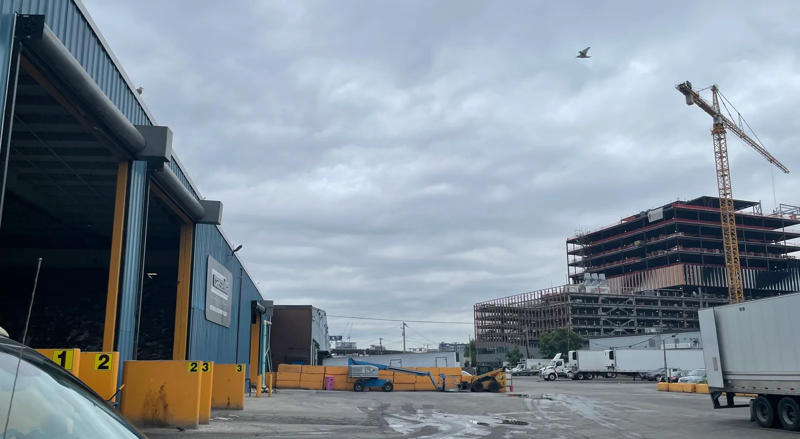 Exterior of industrial building with trucks and large construction crane in the background