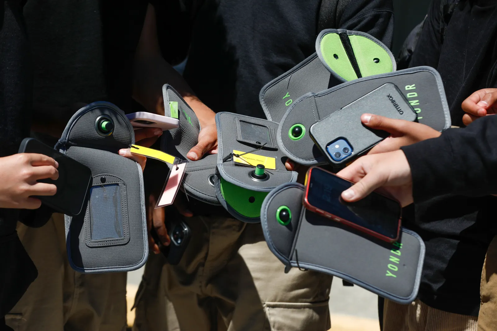People&#x27;s arms and hands are shown holding cellphones and cellphone pouches.