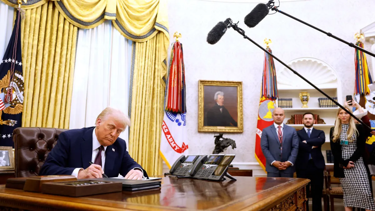 President Trump signs an executive order in the oval office of the white house as staffers and press look on