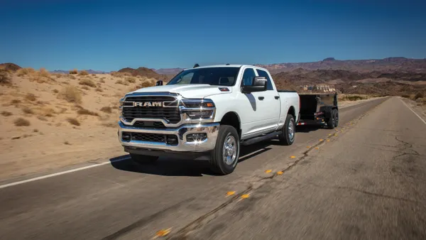 A white 2025 Ram 2500 Heavy Duty Tradesman pickup towing a trailer on desert highway.