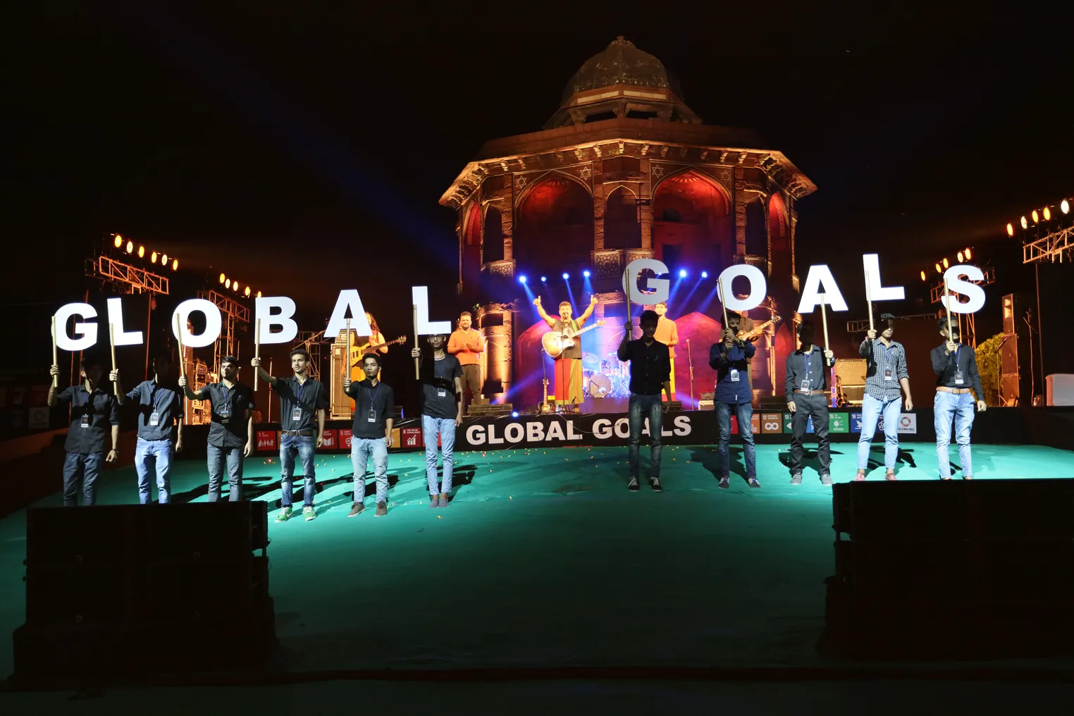 People stand on a green stage each holding one letter of the words Global Goals.