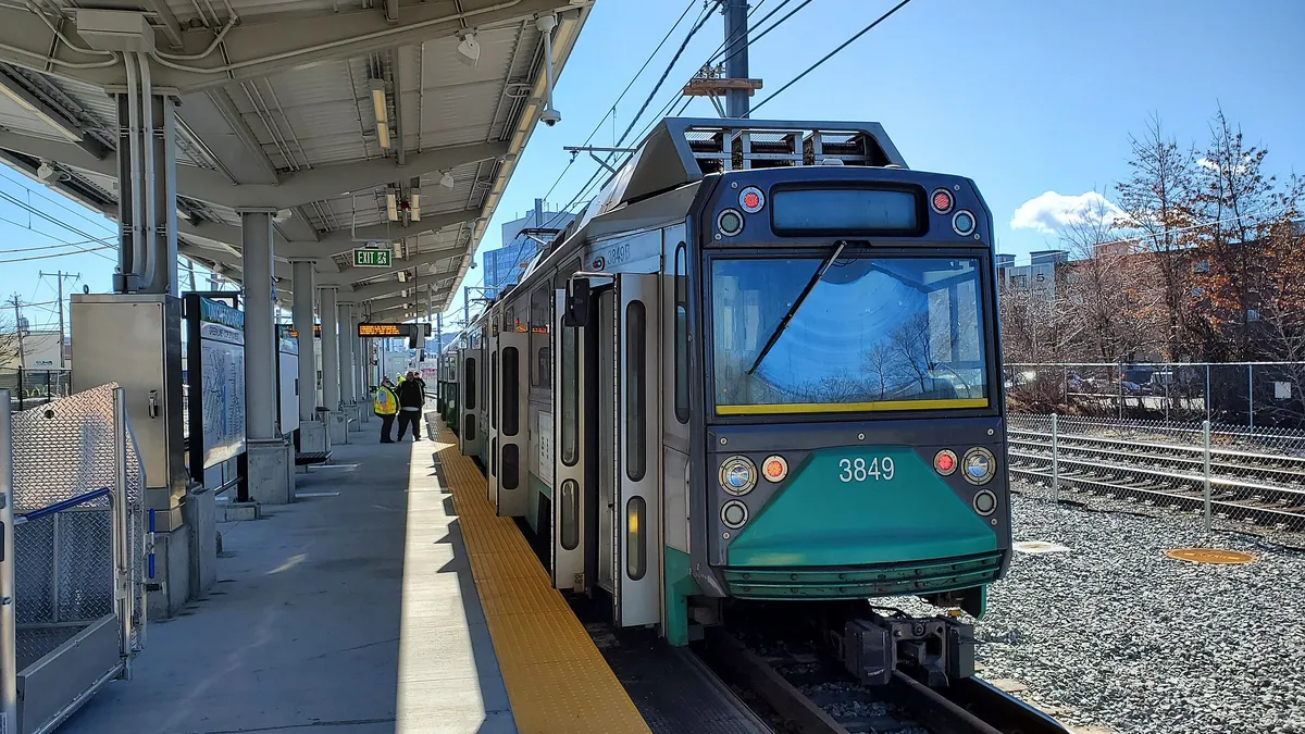 A green train stands on tracks to the right of a new-looking open-air station platform.