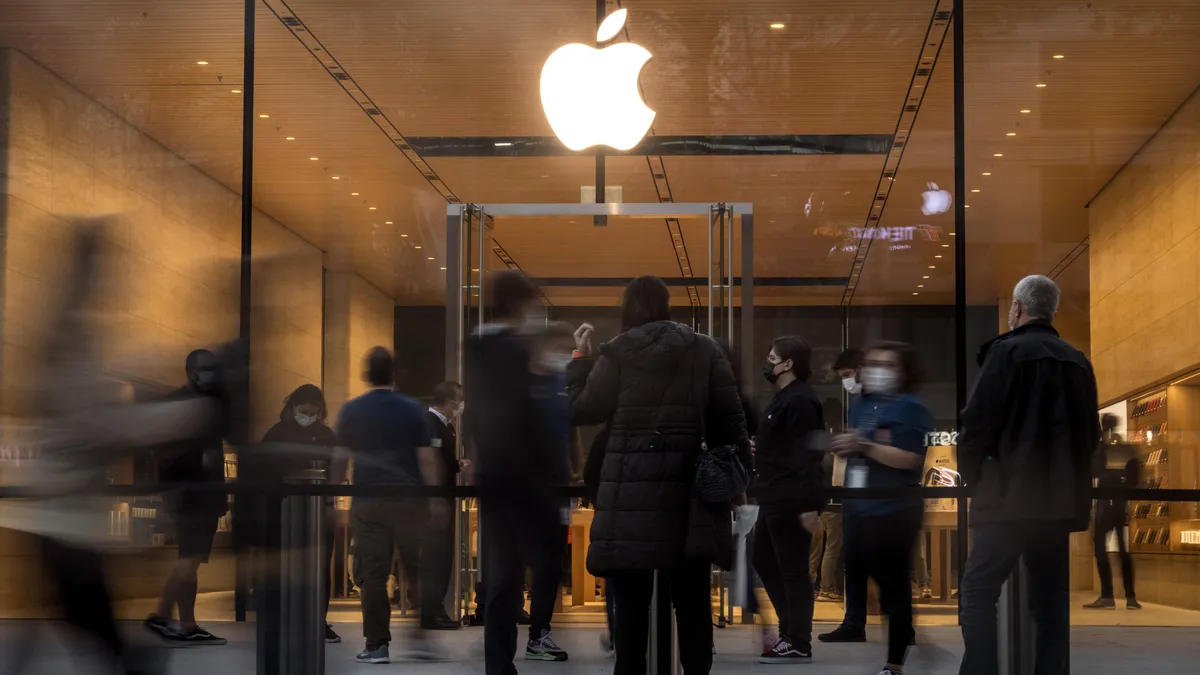 People standing outside a glass storefront with an illuminated apple logo