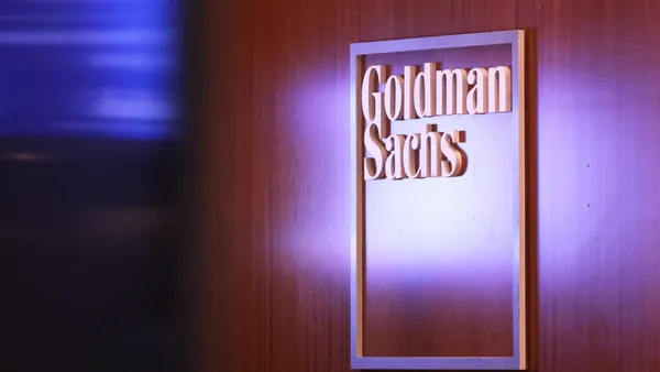 A sign reading Goldman Sachs is seen on a wood-grained wall.