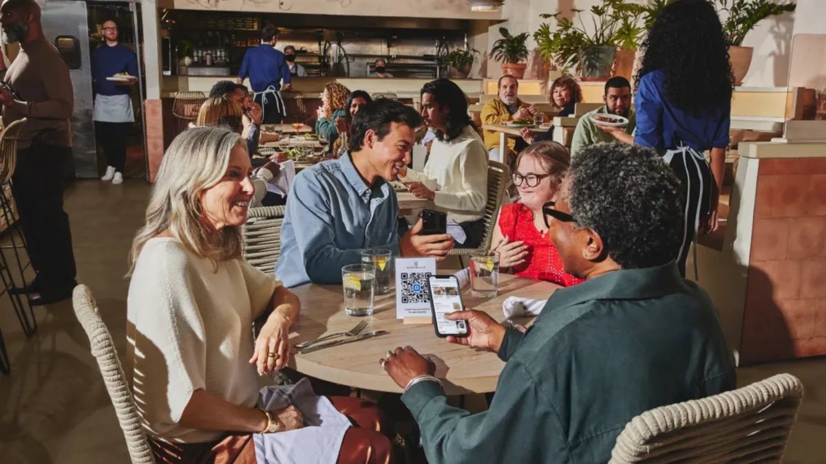 A group of people are enjoying their meal at around a table in a restaurant while one holds a smartphone to a QR tablet in the middle of the table.