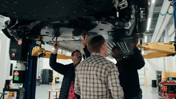 Three Universal EV Platform team members at Ford's Vehicle Performance and Electrification Center working on the underbody shield of a vehicle.