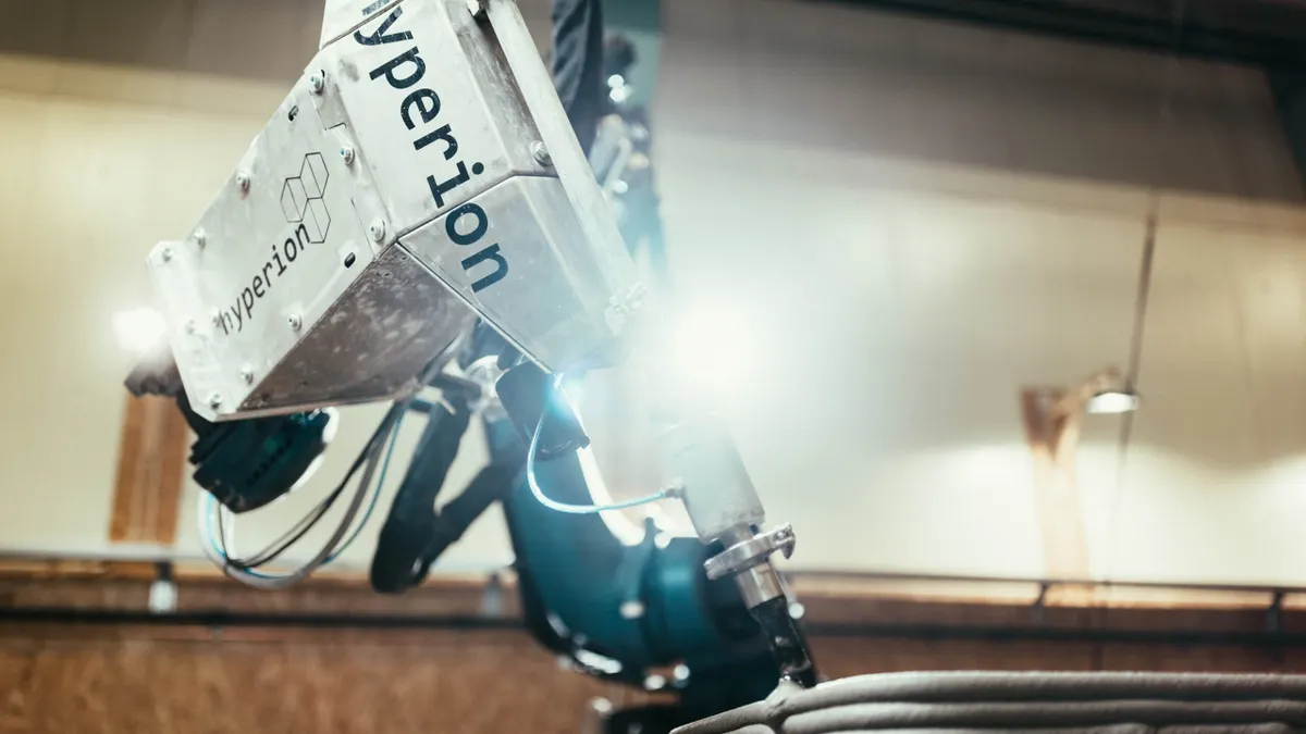 A shot of a robotic arm with a bright flash in the middle. It's funneling a gray mixture out of a tube.
