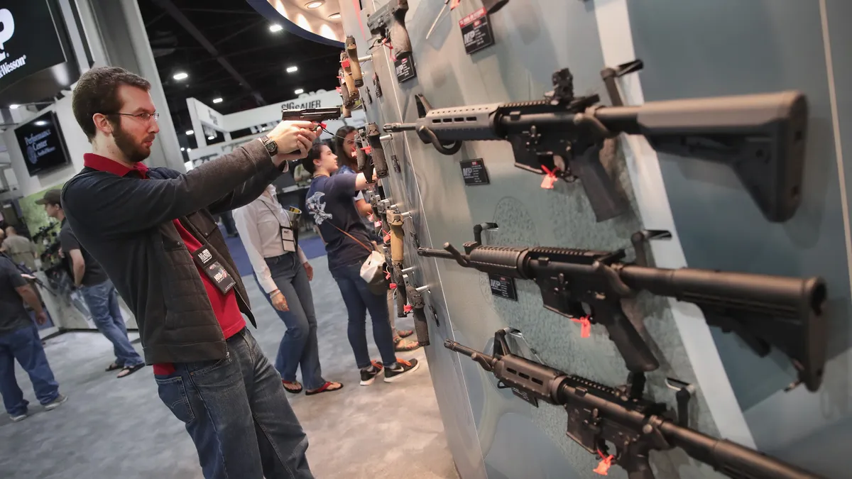 An NRA member holds a pistol while checking out the Smith & Wesson display at an annual NRA convention. The display also includes assault rifles it manufactures.