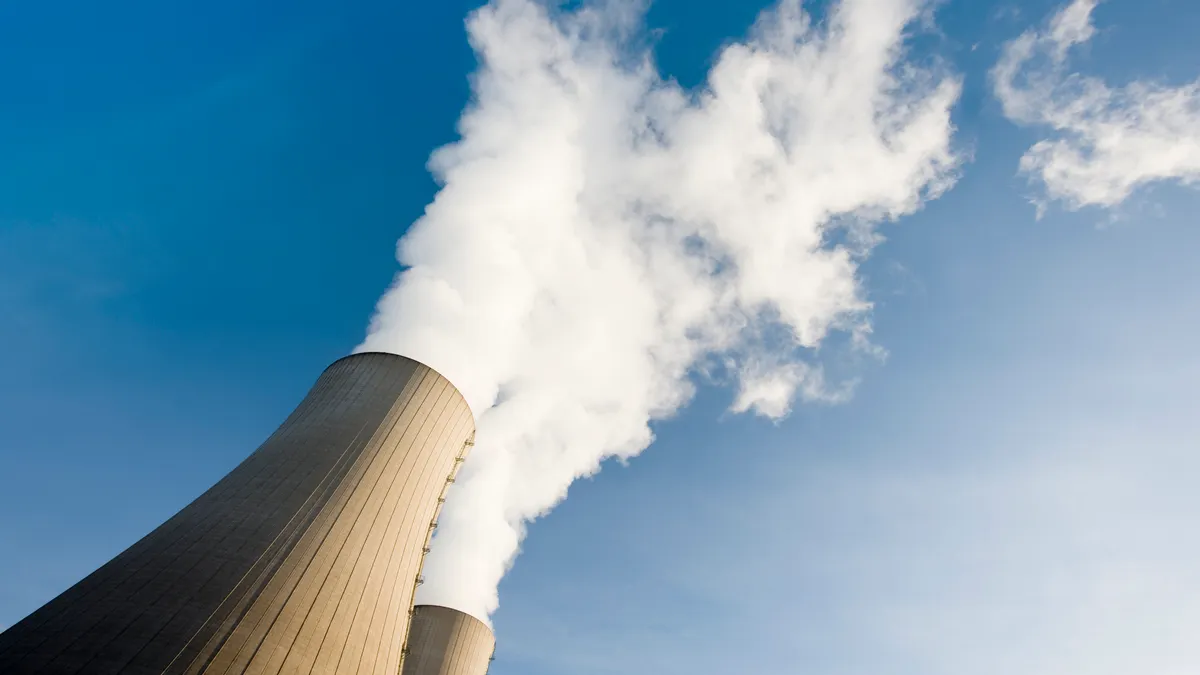 Tilt shot of Two steaming cooling towers for nuclear power against blue sky.