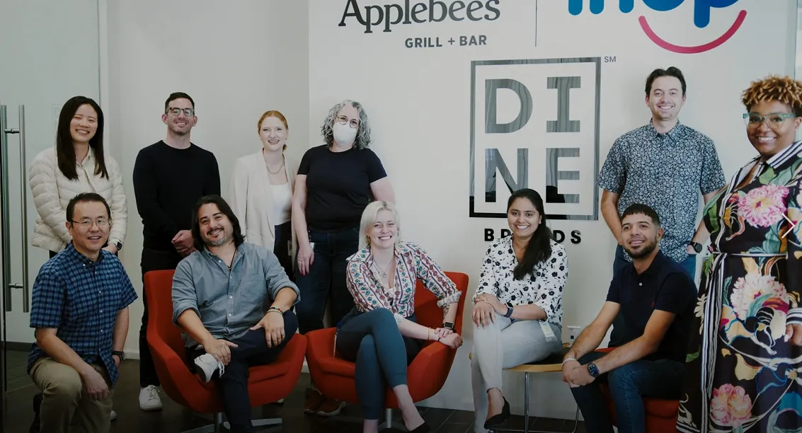 An image of several people standing in front of Dine Brands logo.