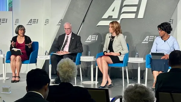 Four people are sitting in chairs on a stage. The letters AEI are shown on a panel behind the people.