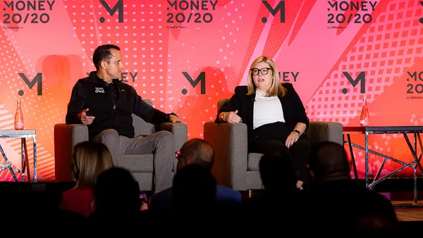 Erin Crawford speaks while sitting on the right side of a stage, in conversation with another person.