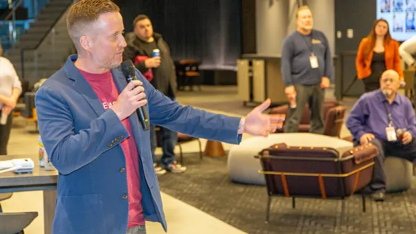 A man with a microphone speaks to a group of seated people encircling him