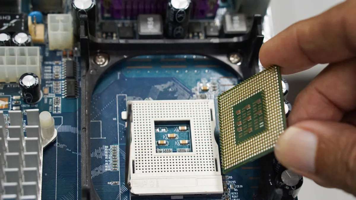 An engineer hands is shown installing a CPU processor into a socket on a computer motherboard.