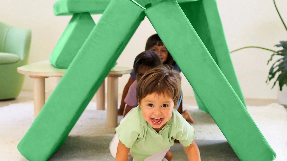 A child crawls through a tunnel made of Nugget couch cushions.