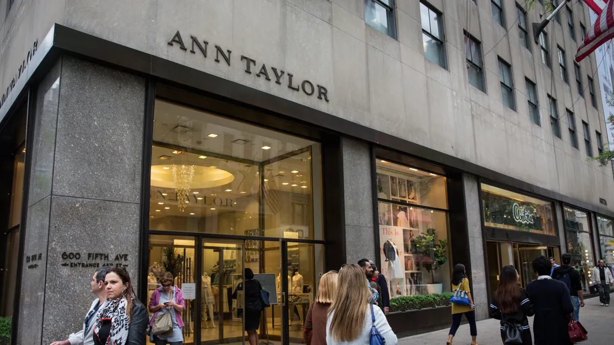 People walking down the street, past an apparel store.