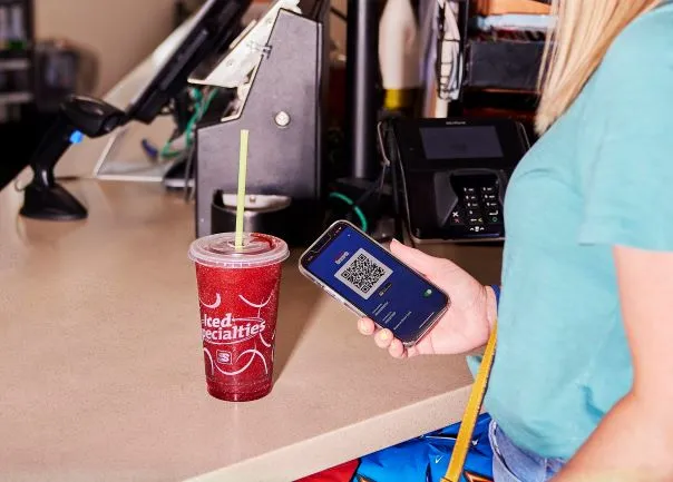 A photo of a dispensed drink on a counter, with a person holding a smartphone next to it.