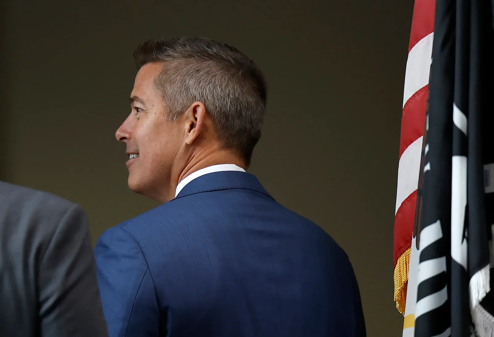 Side view of a man in blue suit standing next to an American flag.