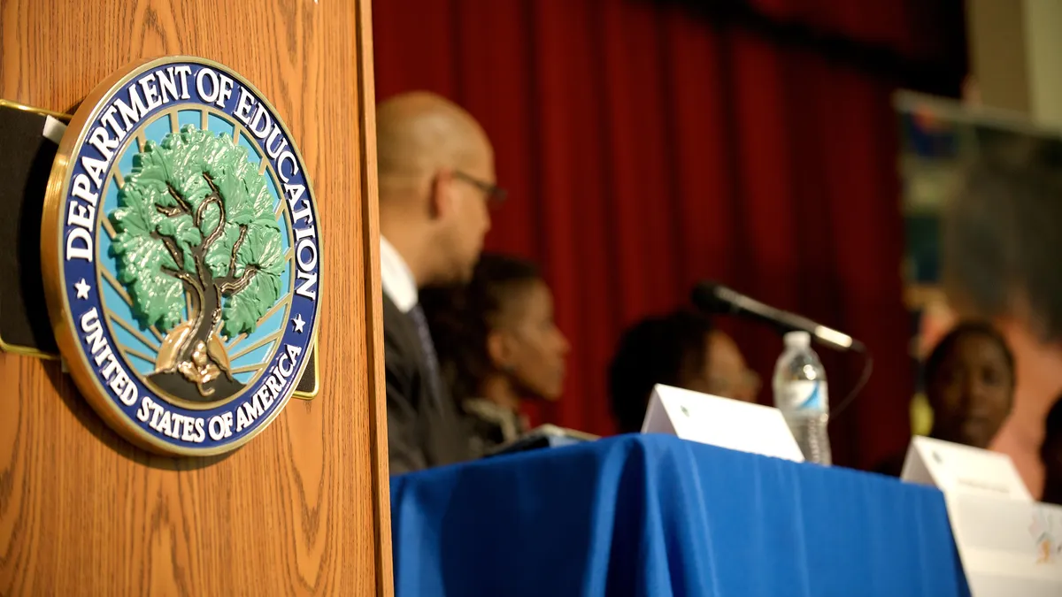 The Education Department's seal can be seen on a podium.