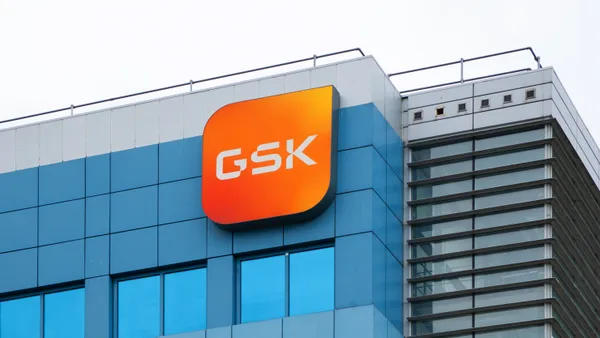 A sign with the letters GSK hangs on the side of an office building.