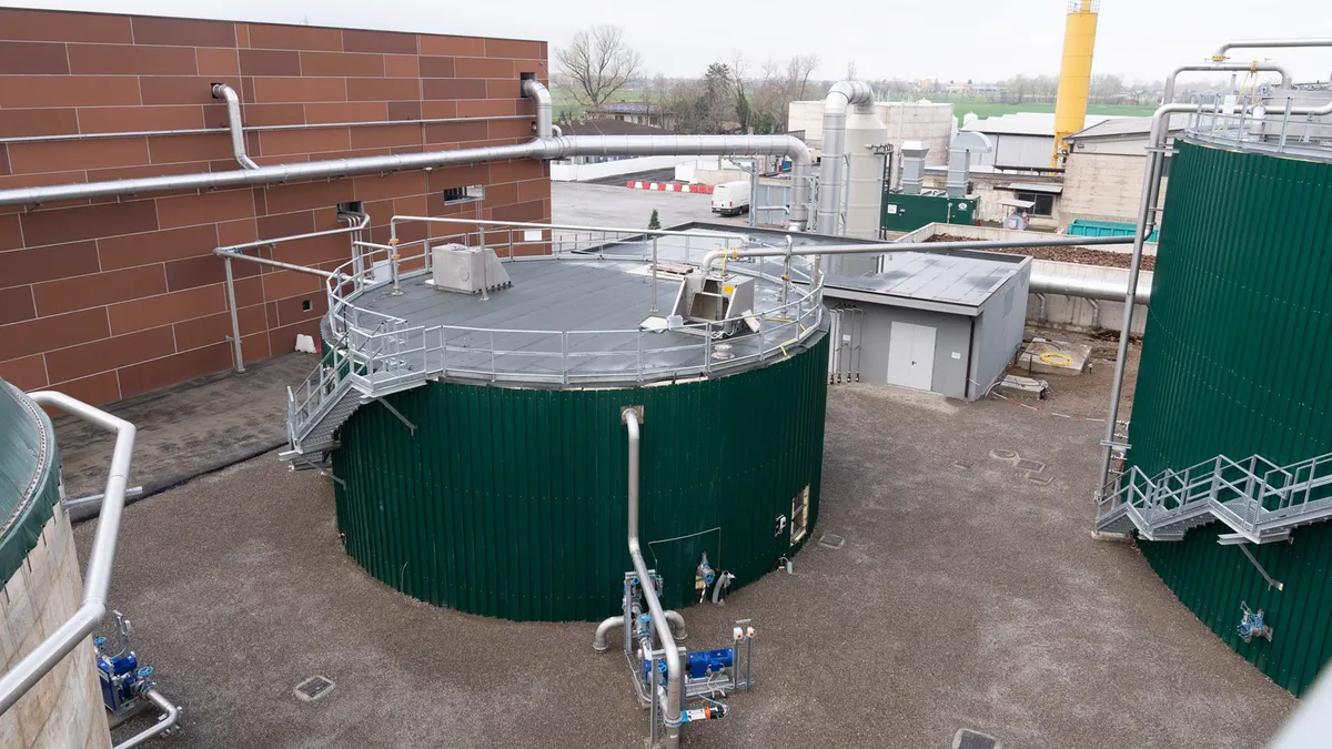 A cylindrical metal tower hooked up to a pipe system in an industrial facility.