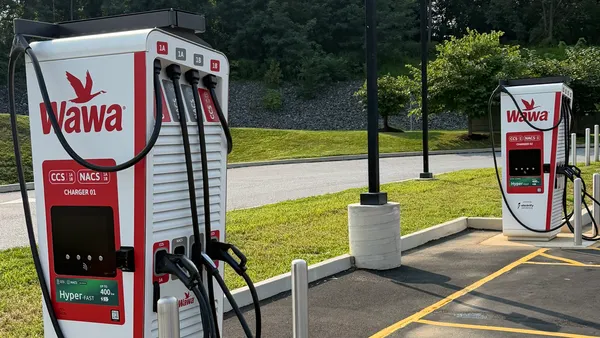 A photo of two electric vehicle chargers in a parking lot. Signs on the chargers say Wawa. CCS. NACS. Hyper-fast.