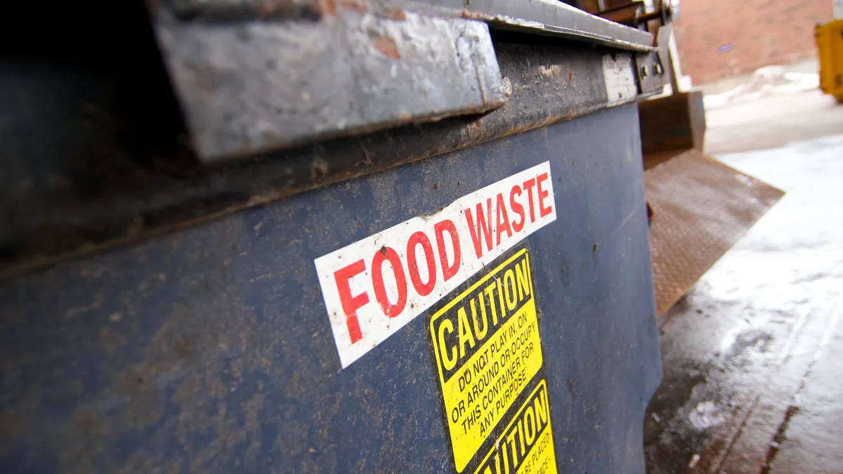 Close-up photograph of a dumpster with a sign that says "food waste"