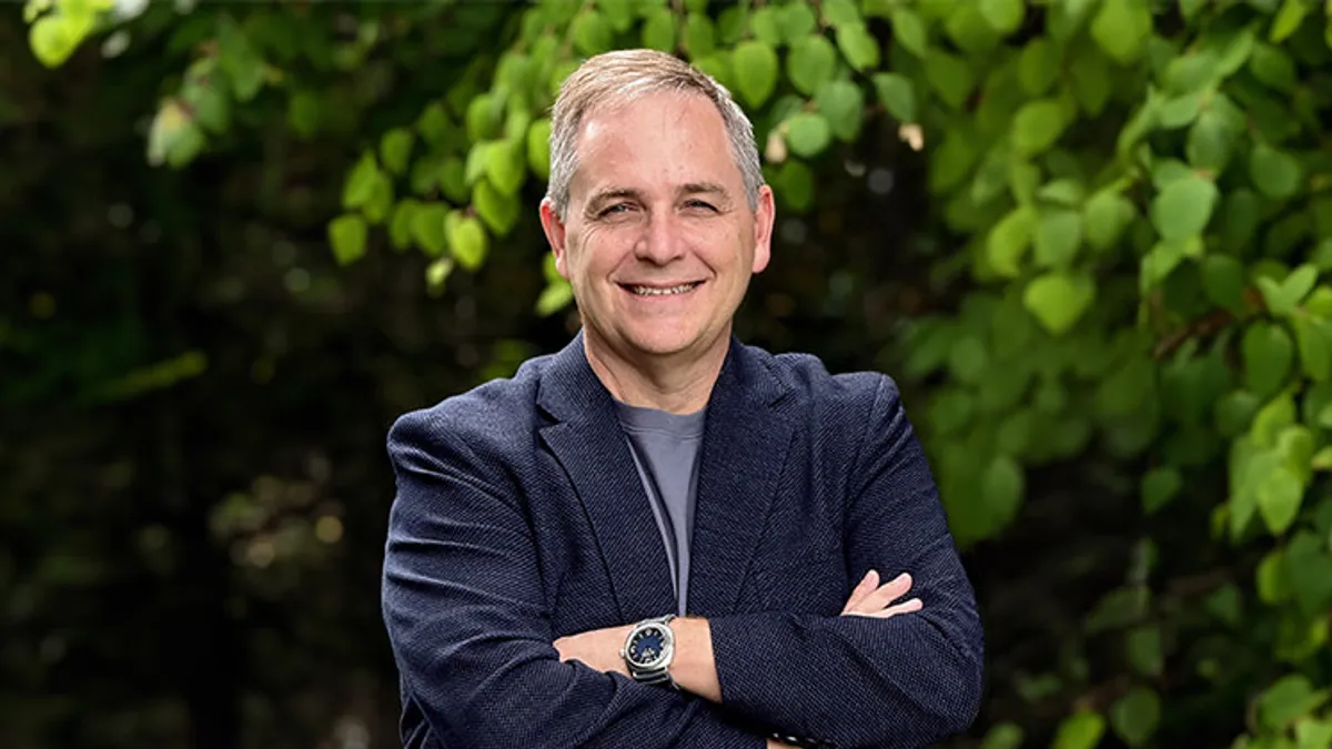 Marc Whitten smiles in a media photo taken outdoors with trees in the background.