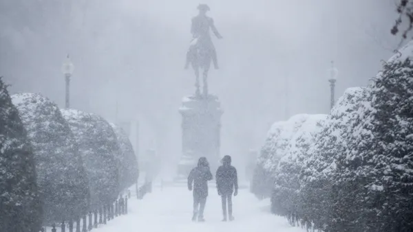 Shadowy figures walk toward a statue of a person on a horse in a snowstorm.
