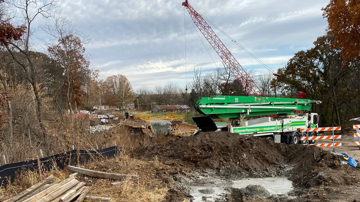 A crane towers over a road with construction machinery and guardrails.