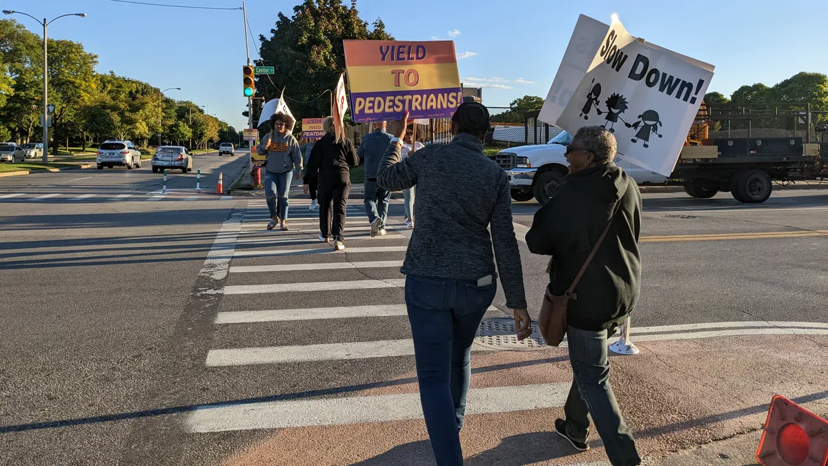 People holding signs cross a street with a green light.