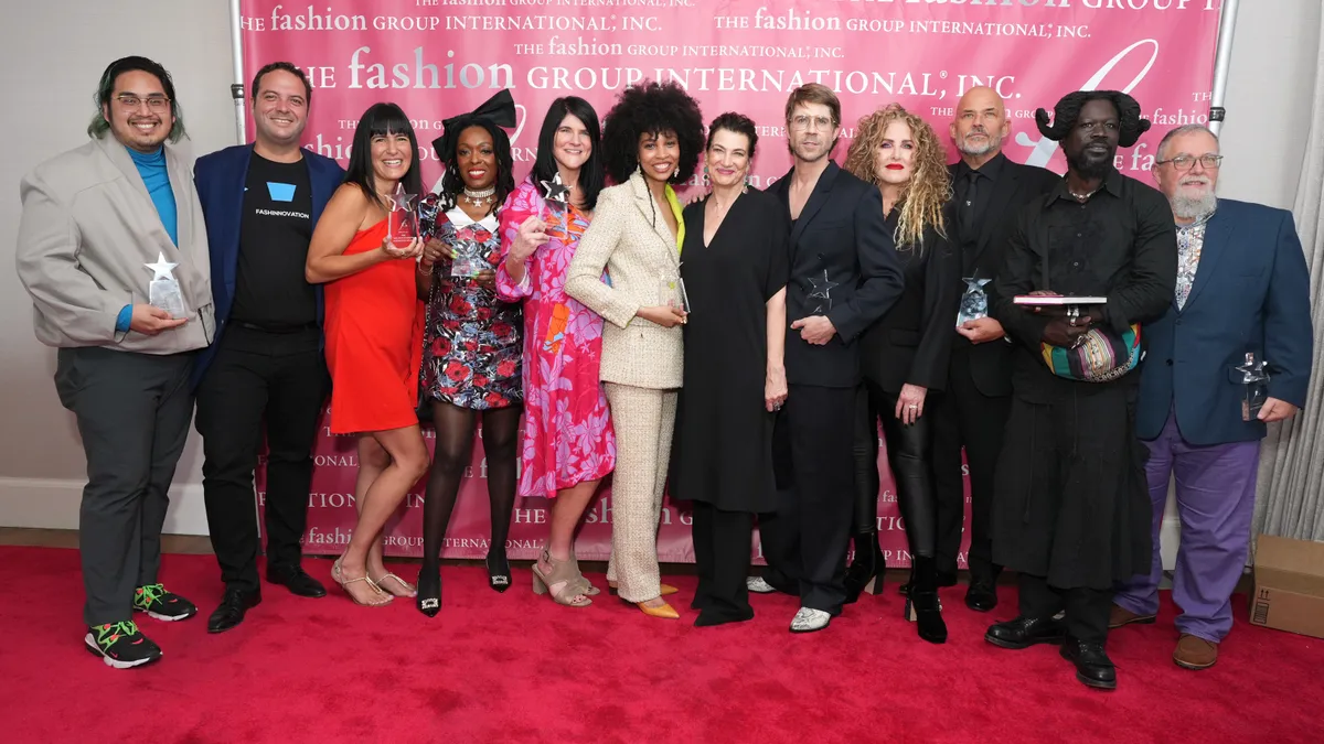 Winners of the Rising Star Awards stand in a line in front of a pink The Fashion Group International banner.