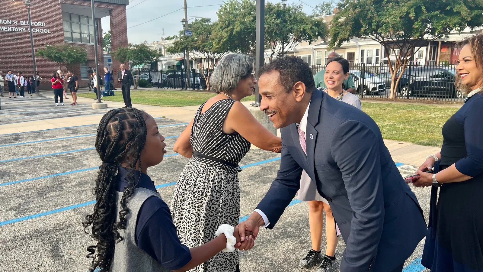 Tony Watlington, superintendent of Philadelphia schools, is pictured shaking the hand of a girl elementary student among other staff on a lot outside a school building.