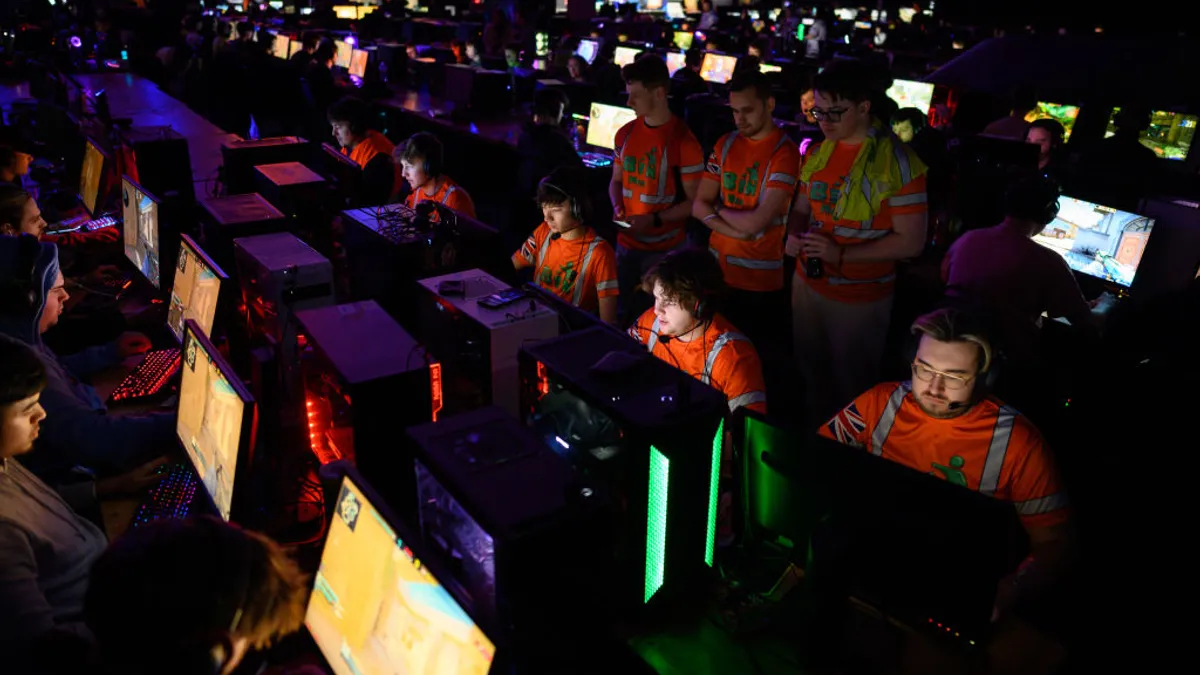 Esports competitors participate in a gaming tournament, seated at rows of computers in a dimly lit theater space.